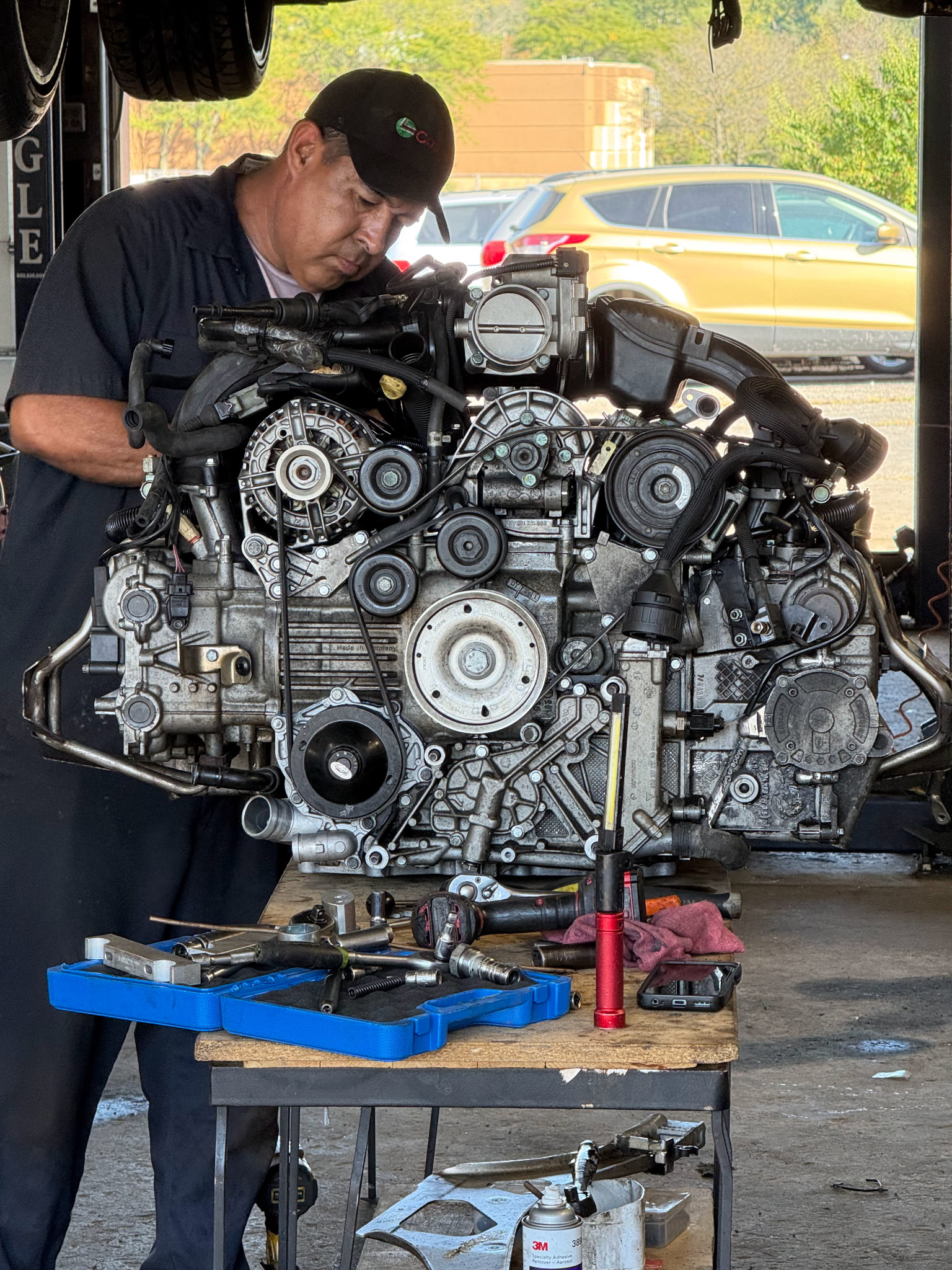 Auto mechanic repairing a car engine at a workshop, inspecting belts and components during a diagnostic service.