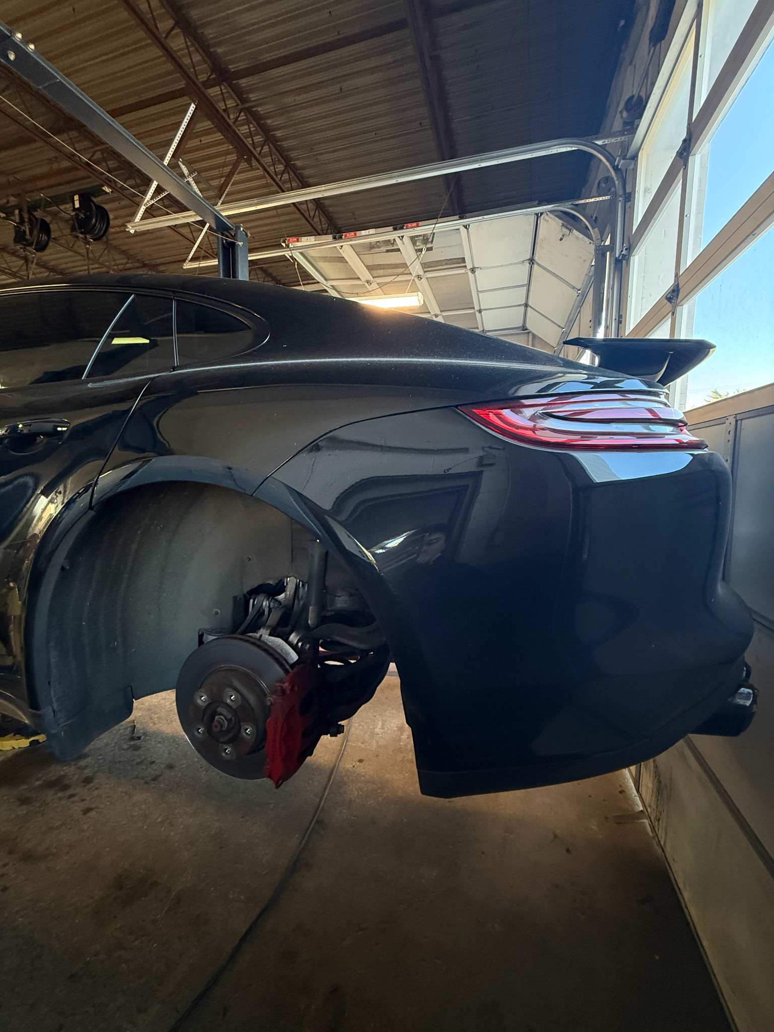 Rear side of a lifted car with the wheel removed at Premier Tire & Autocare, showing the brake assembly and suspension components inside the service bay.