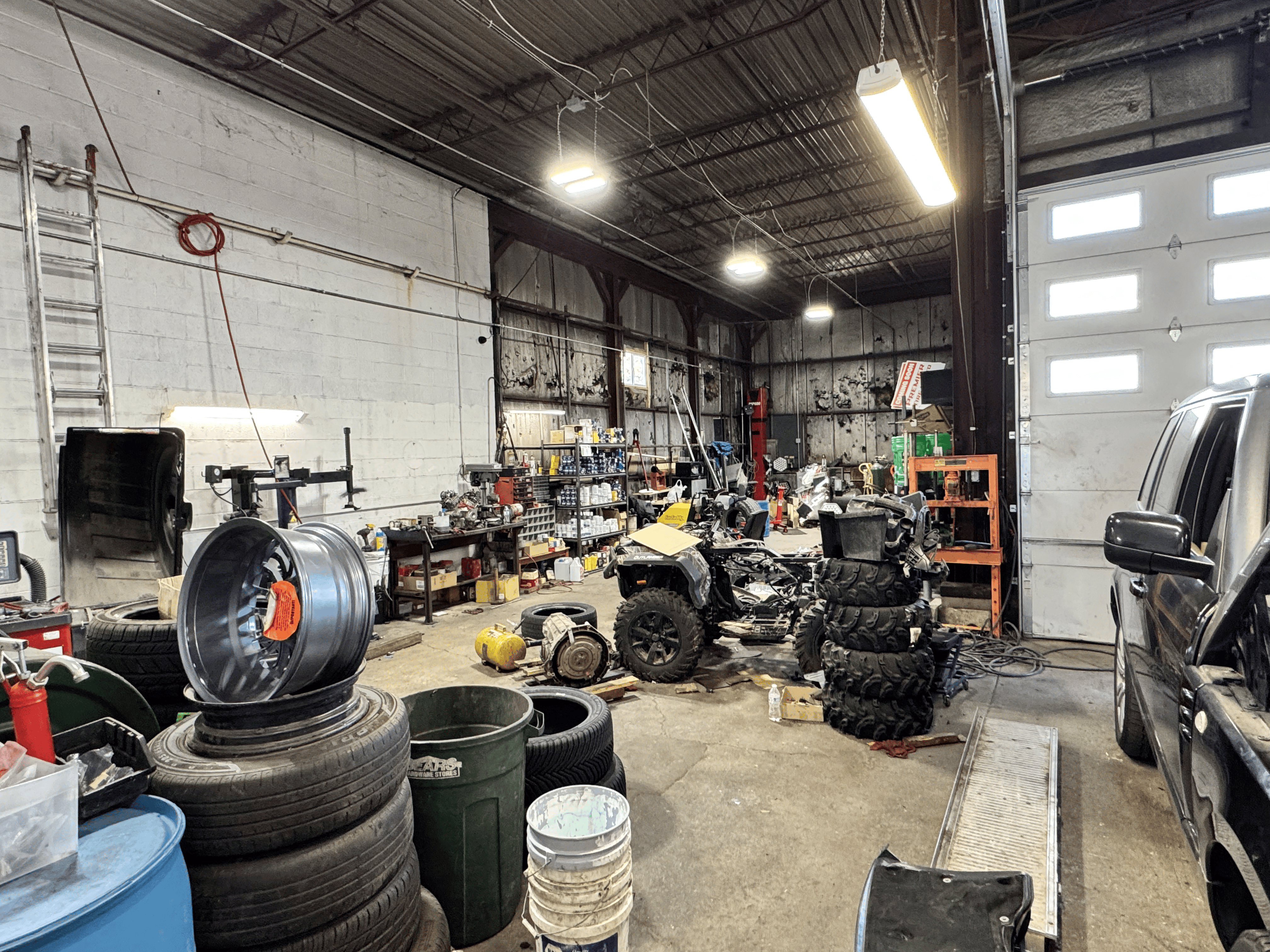 Interior of Premier Tire & Autocare’s workshop with tools, equipment, stacked tires, and ongoing mechanical repairs inside a spacious garage area.